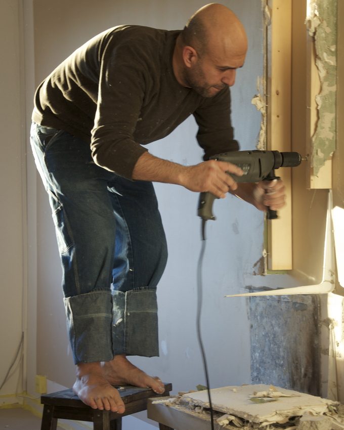A craftsman standing on a stool using a power drill on a window frame