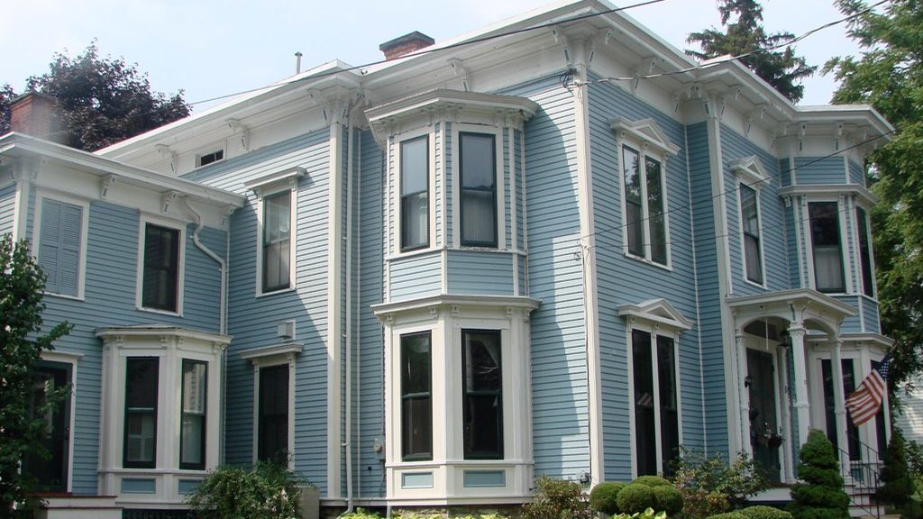 A blue-grey clapboard family home with white trim, bay windows and a tidy front garden