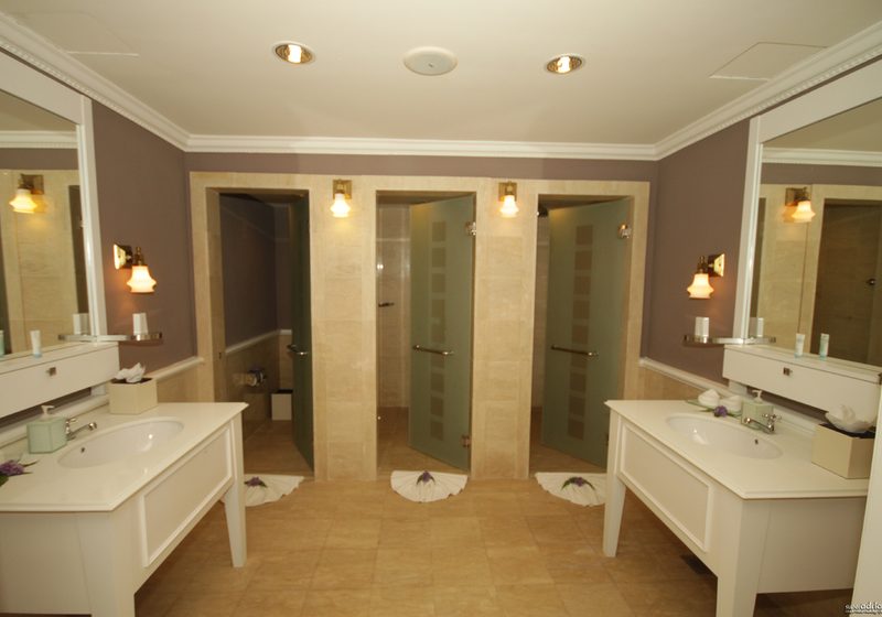 A bright bathroom with twin white vanities, large mirrors and warm wall lights
