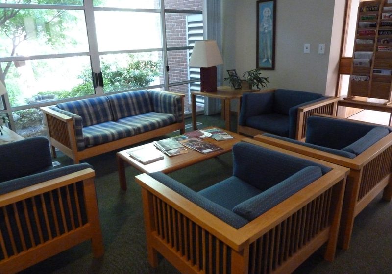 A bright lounge with blue cushioned wooden armchairs and a sofa arranged around a low coffee table