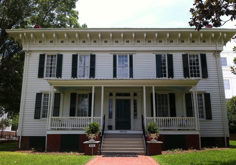 A white two-storey house with black shutters and a long front porch