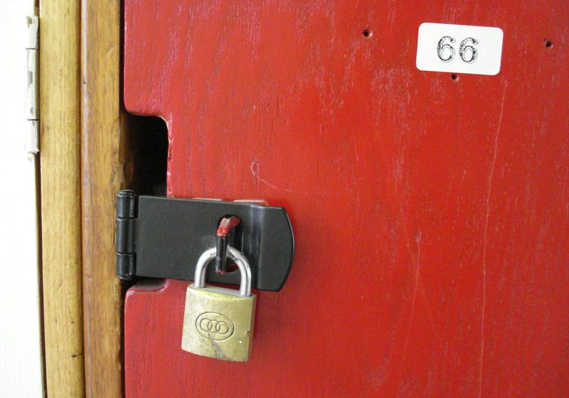 A brass padlock fastened through a steel hasp on a bright red door